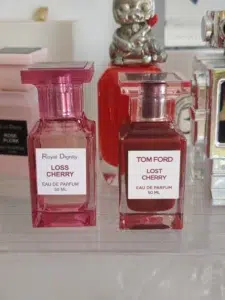 Flacon de parfum de niche hors de prix à côté d'un dupe inspiré par l'ADN olfactif de Lost Cherry et Cherry Smoke.